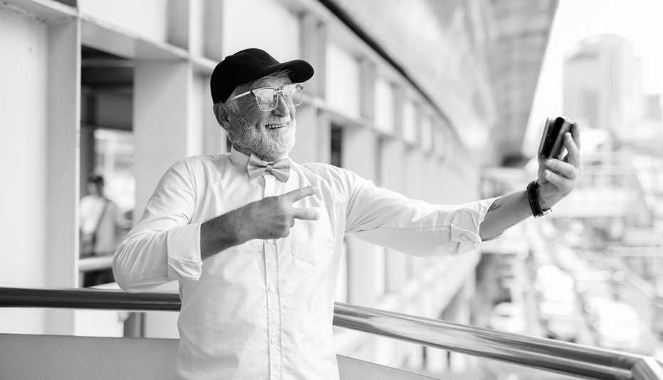 a black and white image of a bearded man smiling and holding up two fingers while taking a selfie
