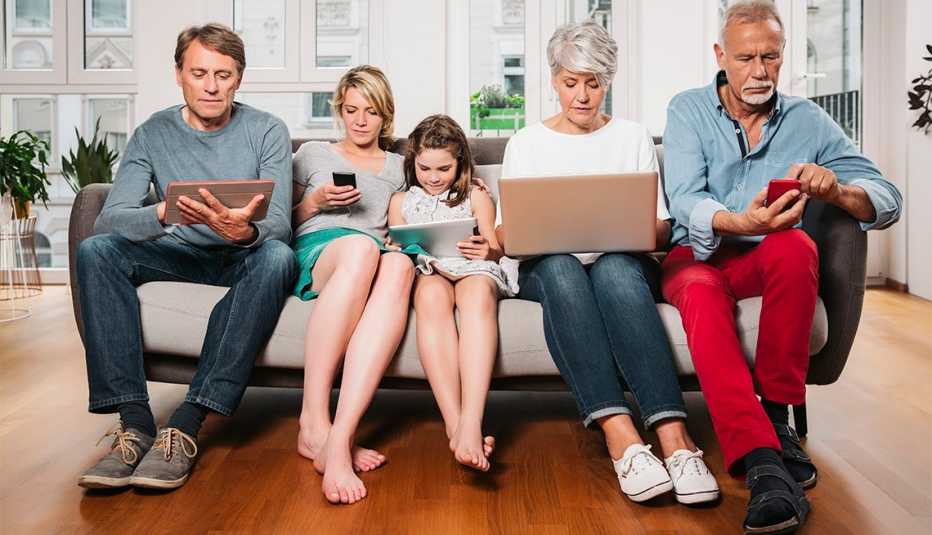 Family of three generations sitting on one couch, busy with one device each, Cologne, NRW, Germany