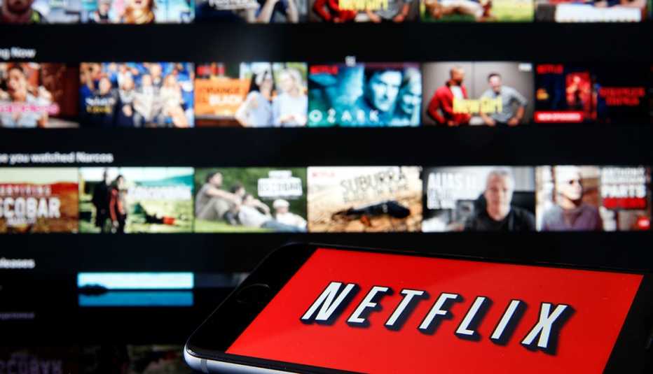 The Netflix logo is displayed on a smartphone in front a television screen that's on the streaming service's home page