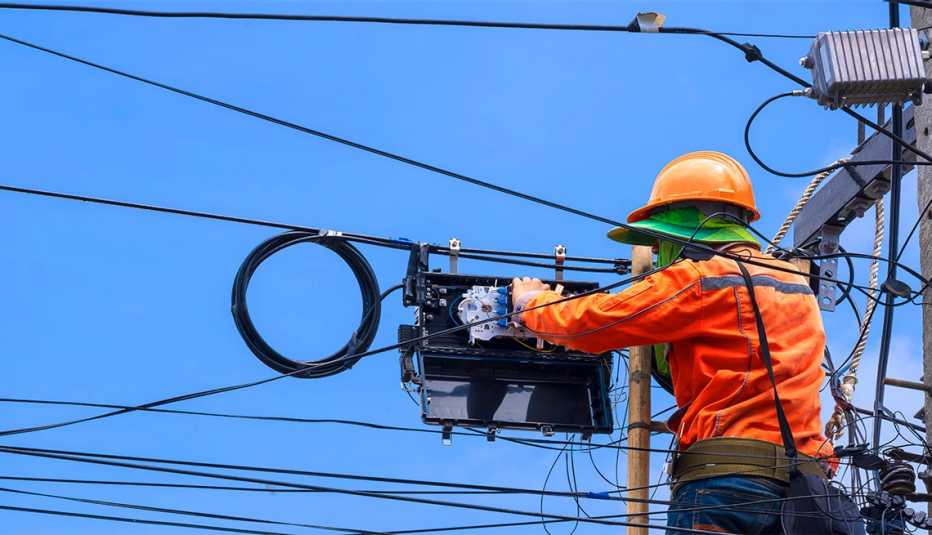 technician on wooden ladder is working to install fiber optic and splitter box on electric pole 