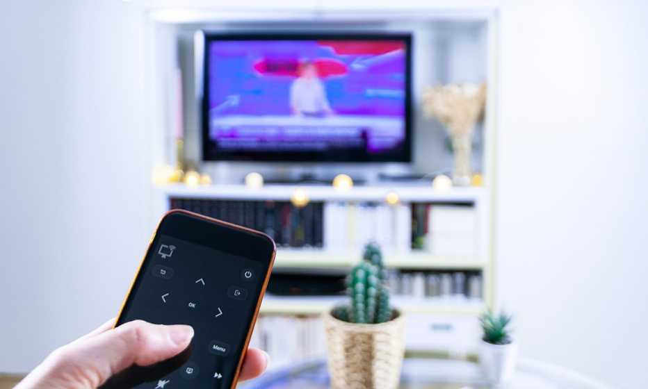 a person uses a smartphone as a remote a woman watches television while using a smartphone as a remote