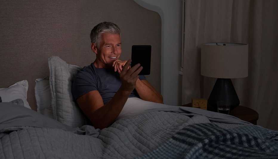 a man smiles while reading on his e-reader in bed a man smiles while reading on his e-reader in bed
