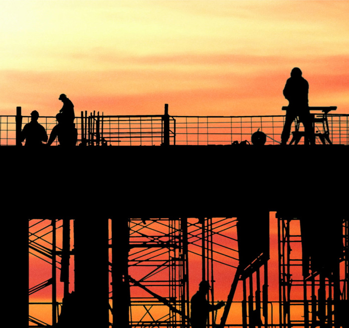 silhouetted construction workers on scaffolding with brilliant orange and yellow sunset in background
