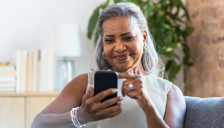 A beautiful senior woman scrolls through social media on her smartphone while relaxing in her home.
