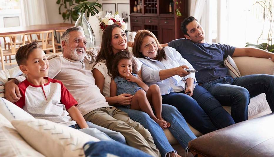 Three generation Hispanic family sitting on the sofa watching TV, grandmother using remote control
