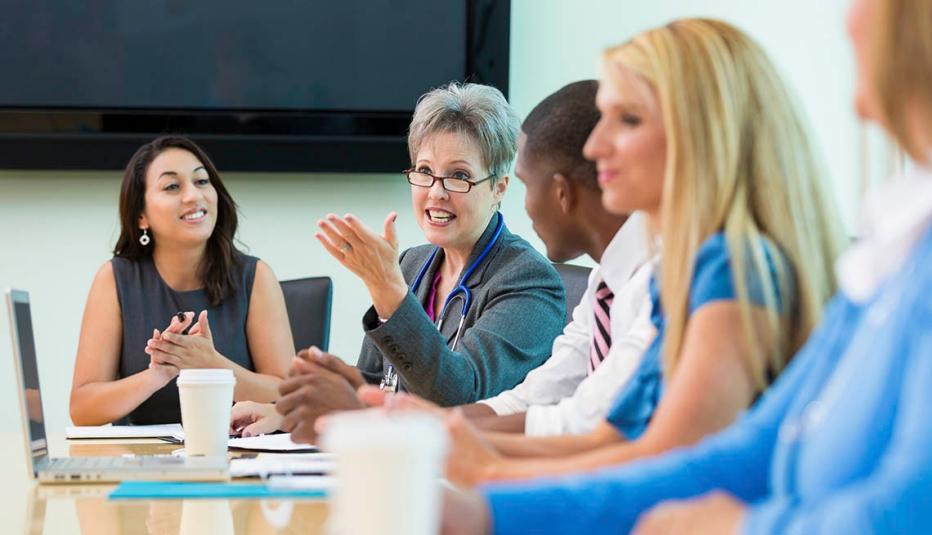Senior female doctor gestures as she talks with doctors and administrators in hospital board meeting. 