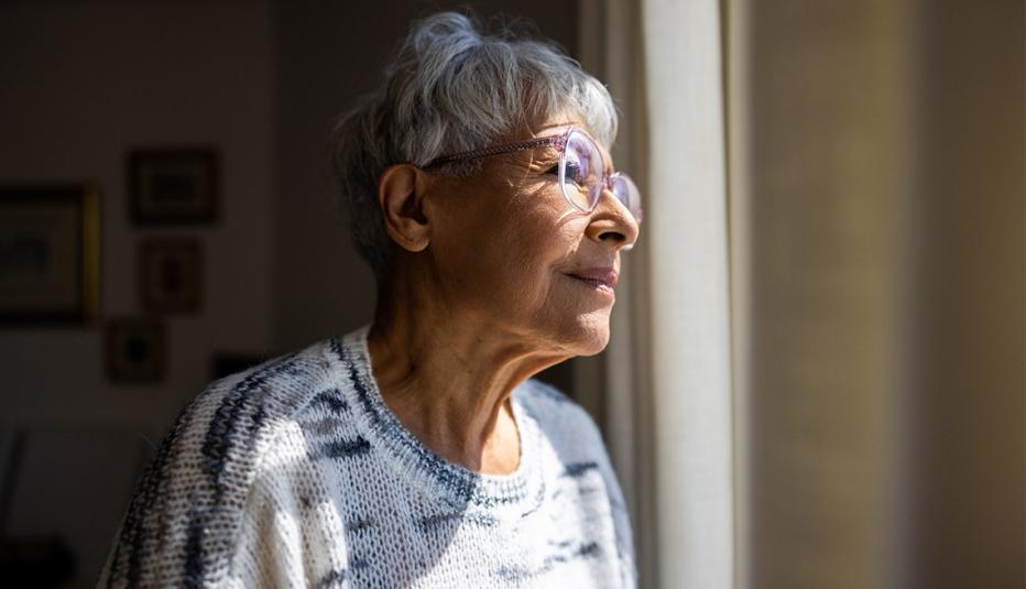 A multiracial senior woman looking out the windows of her home 