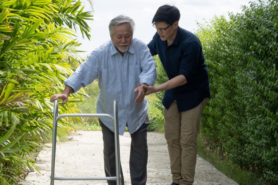young man helping older man using a walker outdoors