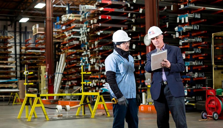 two men in large warehouse wearing hardhats and looking at a building plan