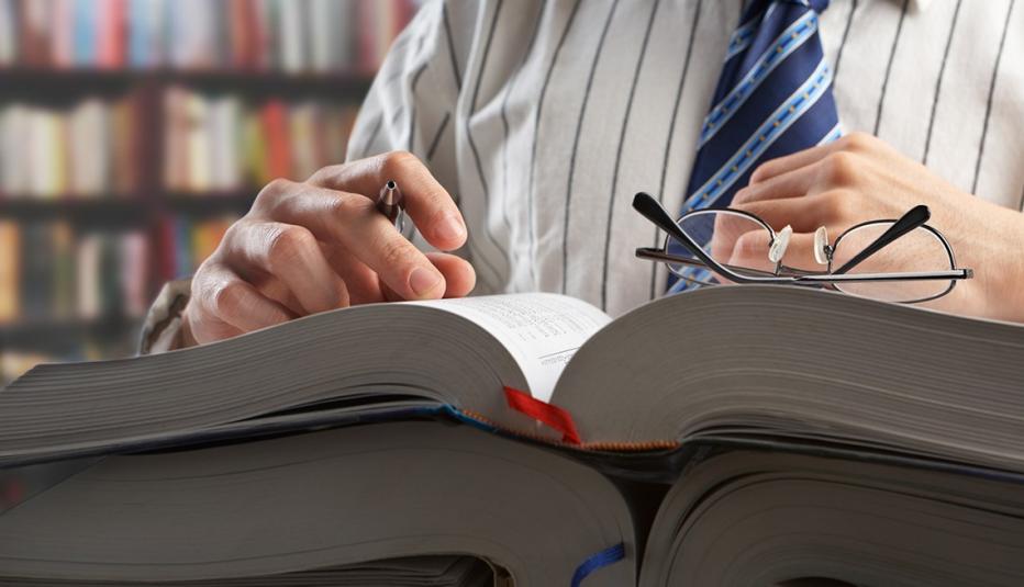 person&rsquo;s hands on open book with eye glasses on book