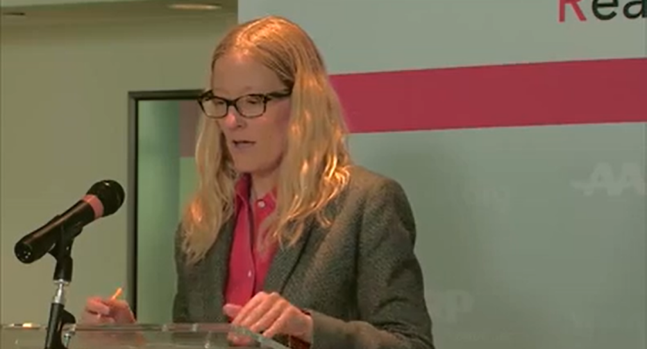 meeting speaker looking at notes on lectern while speaking to audience