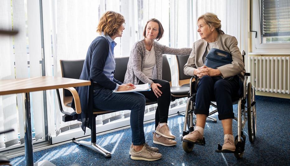 A doctor having a discussion with a woman in a wheelchair and her adult daughter