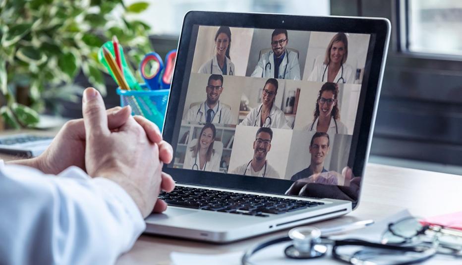 close up of a doctor's hands sitting on his laptop as he watches a video conference call with other doctors
