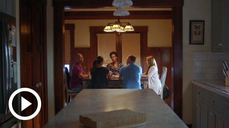 people sitting around table view from far away, with video icon on bottom left