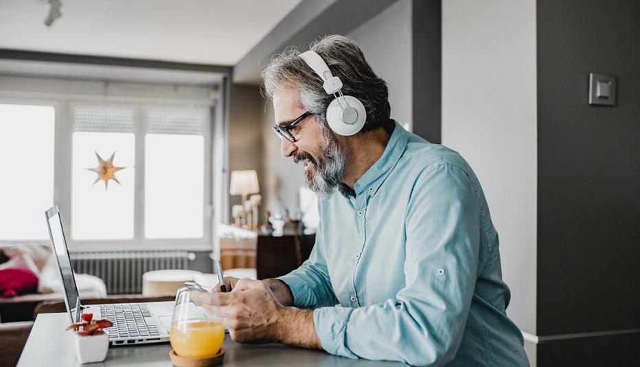a man at a laptop with his headphones on and holding a pen and paper