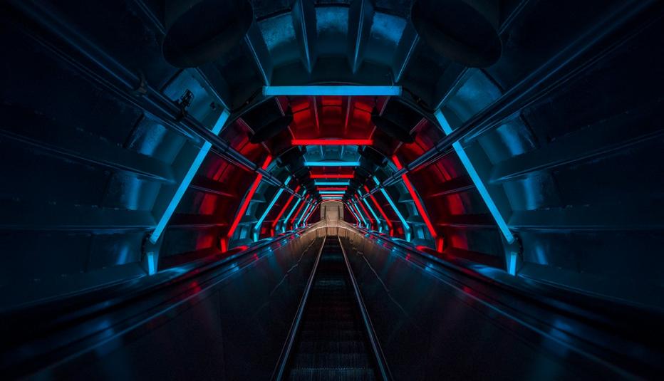 Long escalator inside a subway tunnel surrounded by red and blue lights Long escalator inside a subway tunnel surrounded by red and blue lights