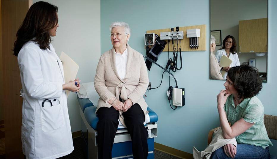 Female patient sitting on exam table in discussion with her doctor and adult daughter