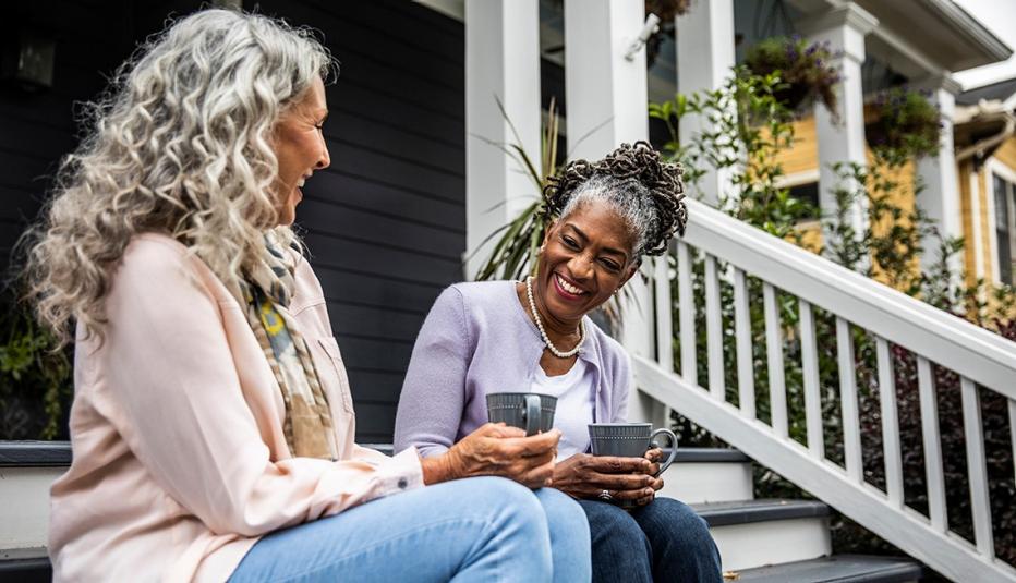Senior women having coffee on the front steps of a suburban home.