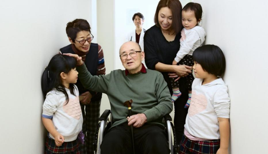 Hospital discharges Asian man for home treatment. His family warmly celebrates and the doctor looks relieved standing behind in the background.