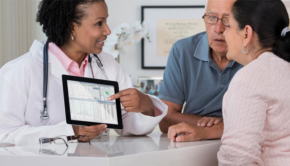 Doctor showing a digital tablet to patients sitting at a table in a doctor's office.