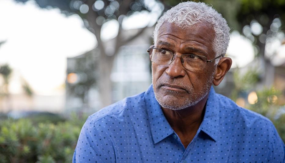 Older black man with white hair, glasses, and a blue shirt sitting outside.
