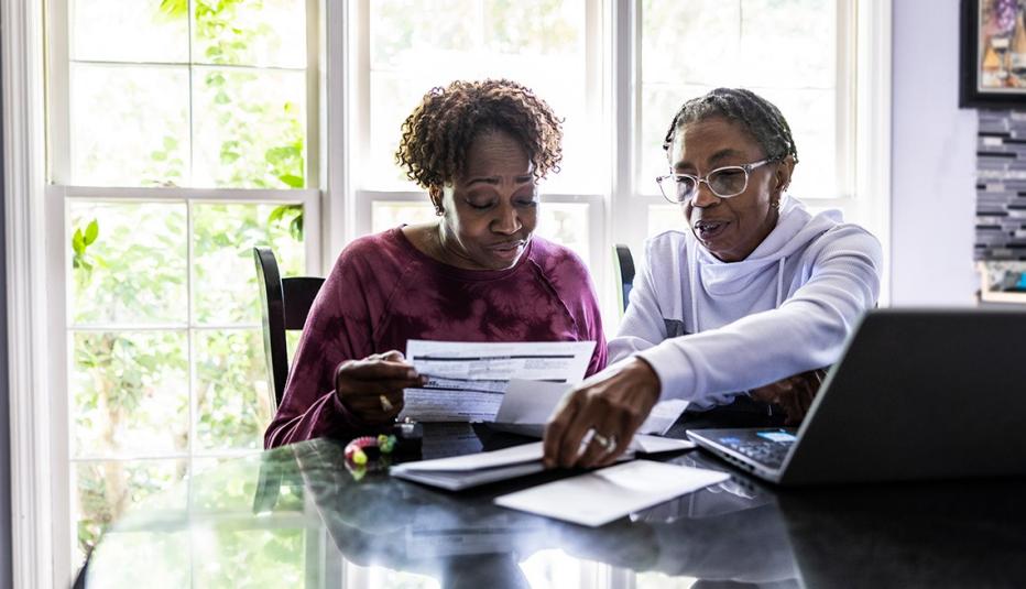 Lesbian couple paying bills and using laptop at kitchen table 