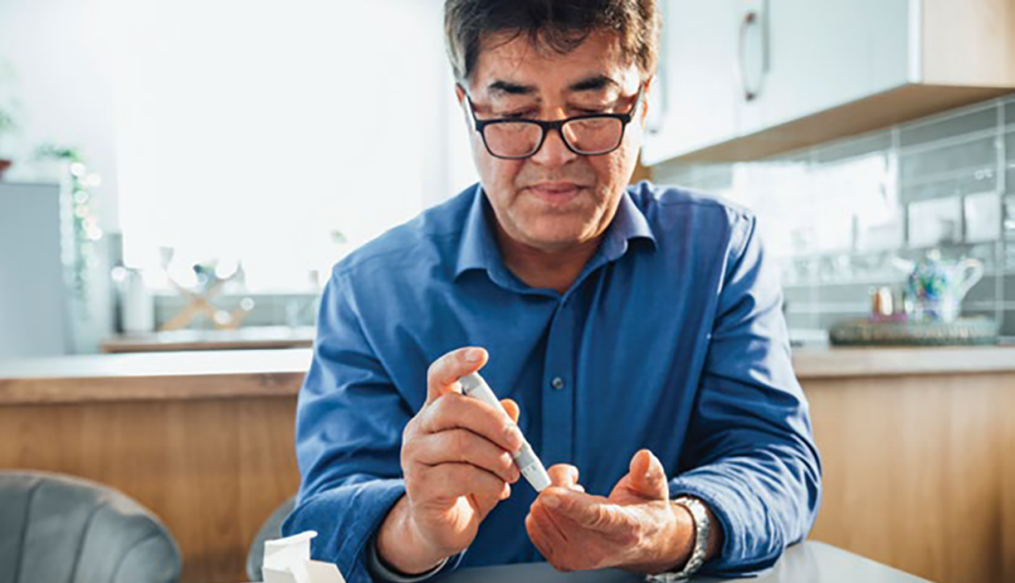 man sitting at table pricking his finger using a glaucometer to test his blood sugar level