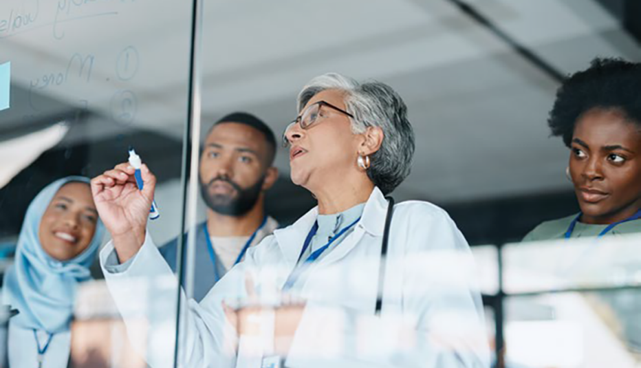 doctor writing on clear board with others looking on in background