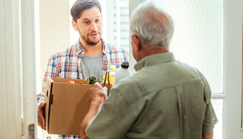 A young adult volunteer giving a box of fresh groceries to man