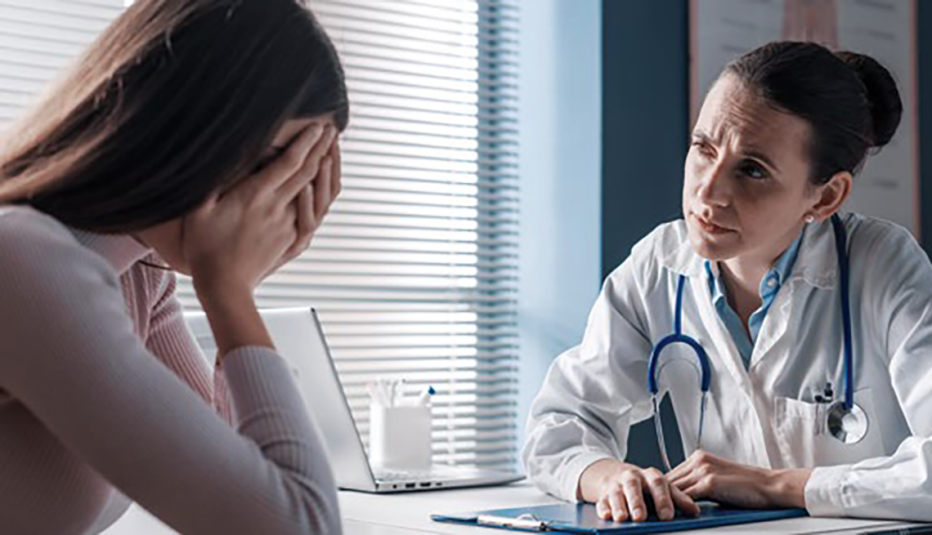 concerned doctor facing a woman with her head in her hands at a table