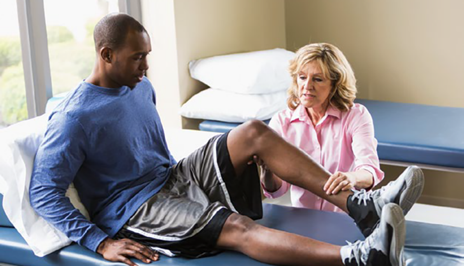 physical therapist helping man seated on therapy table with his leg