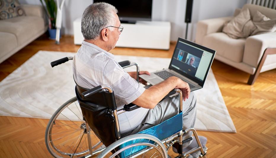 older man sitting in wheelchair, using laptop for telehealth appointment with doctors.