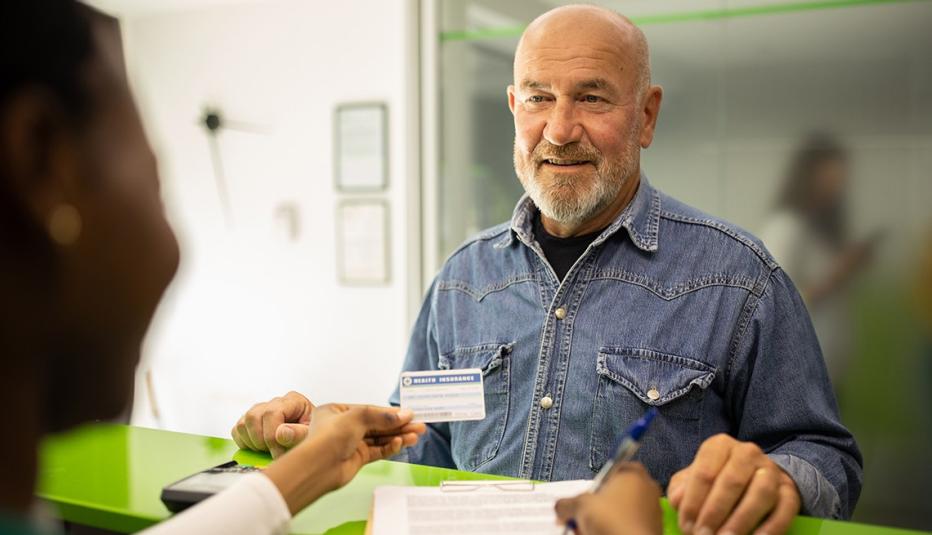Older white man is signing papers at a high counter in doctor's office.