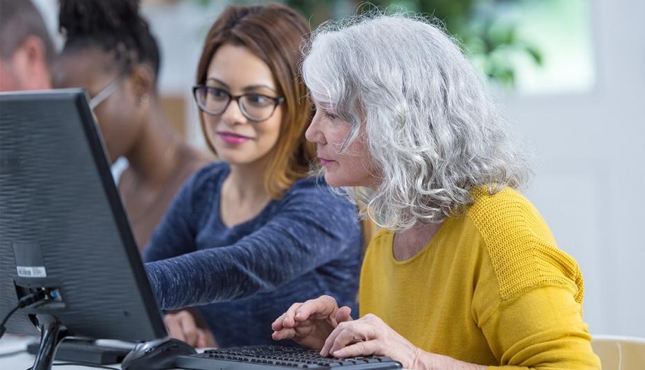 A younger woman shows an older woman something on a desktop computer.