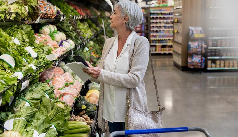 Data Visualization: 1 in 10 Adults Ages 50 and Older Were Food-Insecure in 2023 Mature woman holds smartphone while shopping for leafy greens in local supermarket.