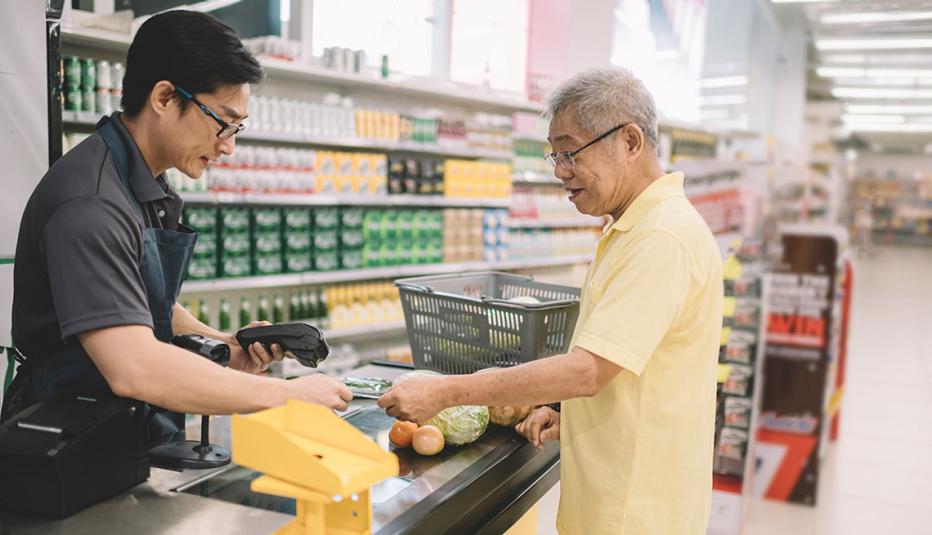 An Asian senior adult paying for his shopping items to cashier at counter check out in supermarket An Asian senior adult paying for his shopping items to cashier at counter check out in supermarket