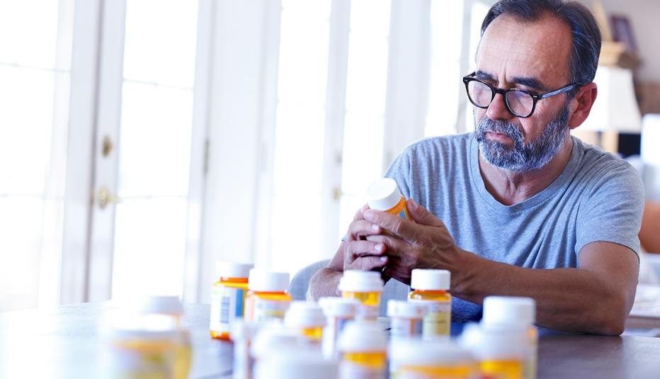 Drug Disposal Report A latino baby boomer sits at his dining room table and sorts through various prescription medications as sunlight filters in through the window behind him bathing the room with a soft glow of light.