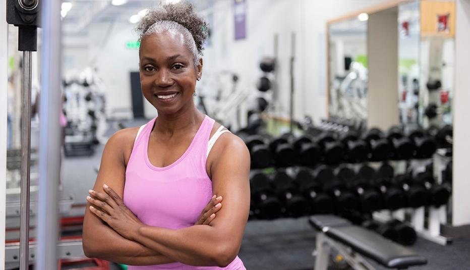 Woman at the gym standing in front of the barbell rack with her arms folded and smiling.