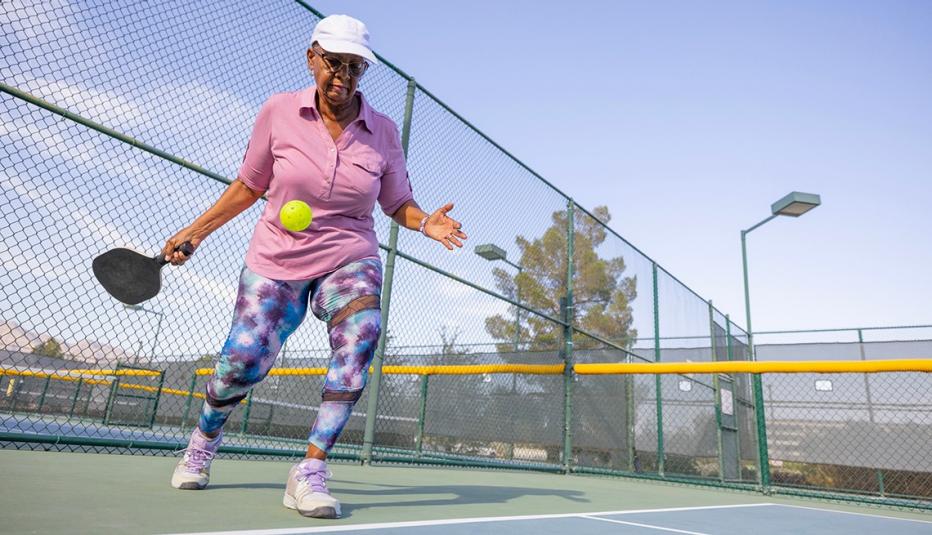 Stop action photo of a woman dressed in athletic gear preparing to hit a pickleball on a pickleball court.