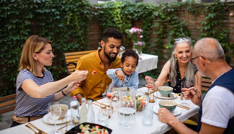 A diverse family eating a meal outside on a fenced in patio