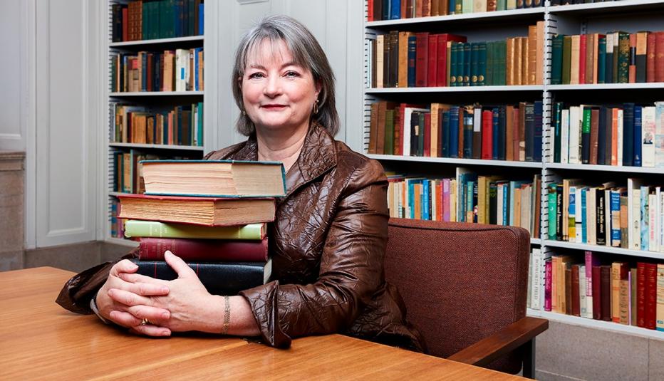 Siobhan Reardon sitting at table holding stack of books.