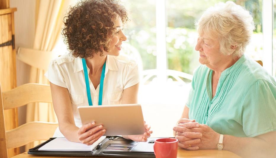 a care worker or medical professional or housing officer makes a house call to a senior client at her home . She is discussing the senior woman’s options on her digital tablet.