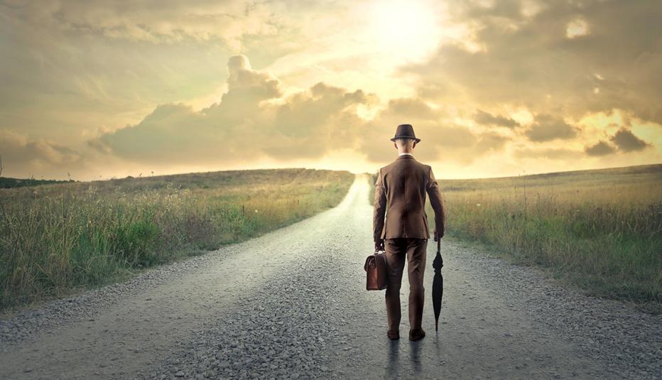 Man walking alone down a road holding briefcase and umbrella