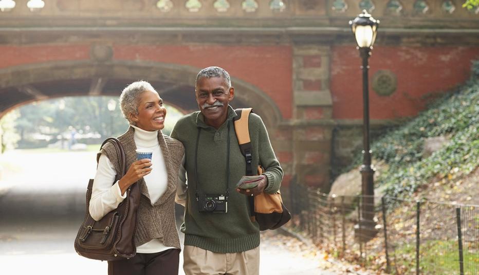 Couple walking through a park in New York City. A bridge is in the background Couple walking through a park in New York City. A bridge is in the background