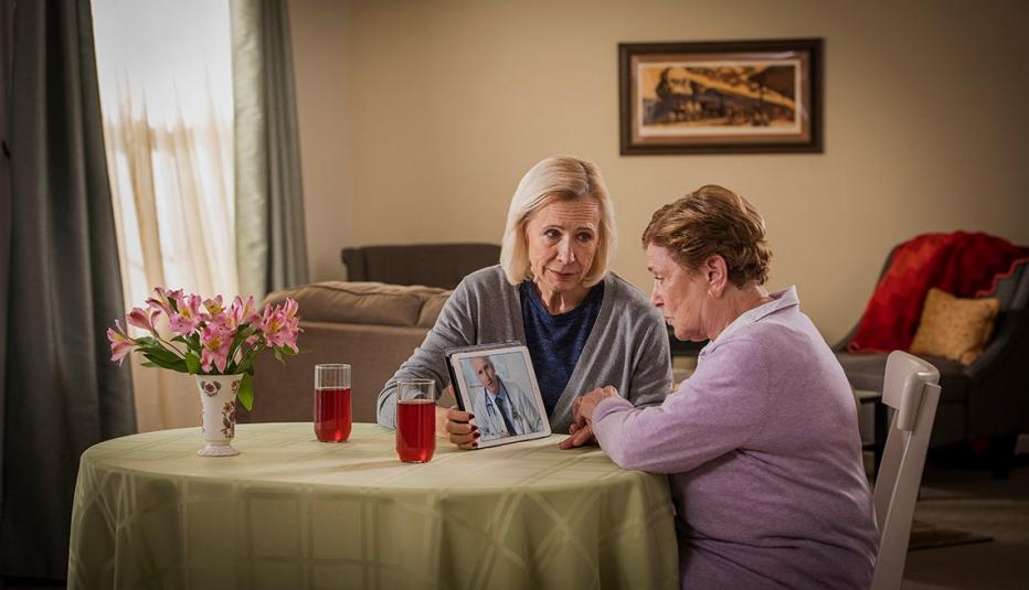 Daughter assisting her elderly mother with a telehealth video call with a doctor