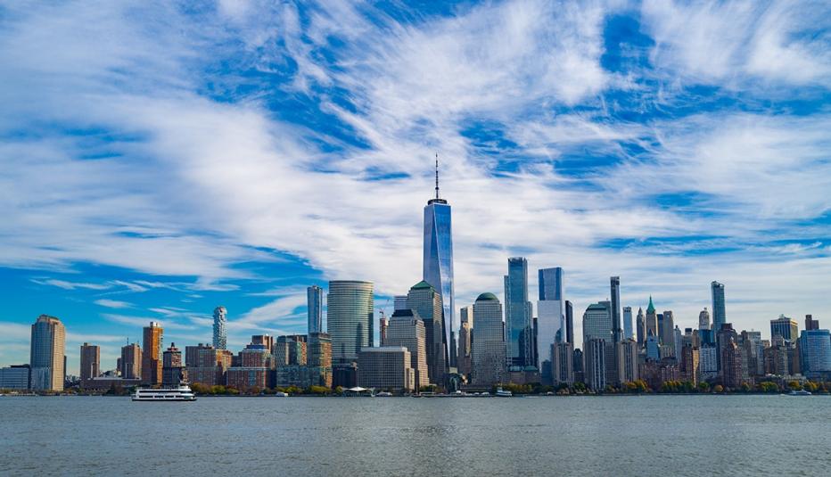 View of the New York City skyline from the harbor, with wispy clouds in a blue sky.