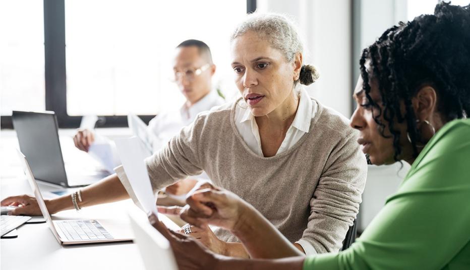 May 2025 Employment Data Digest Two mature business women sitting at desk using laptop and discussing important document. Female office workers studying paperwork in office, collaboration, strategy, teamwork