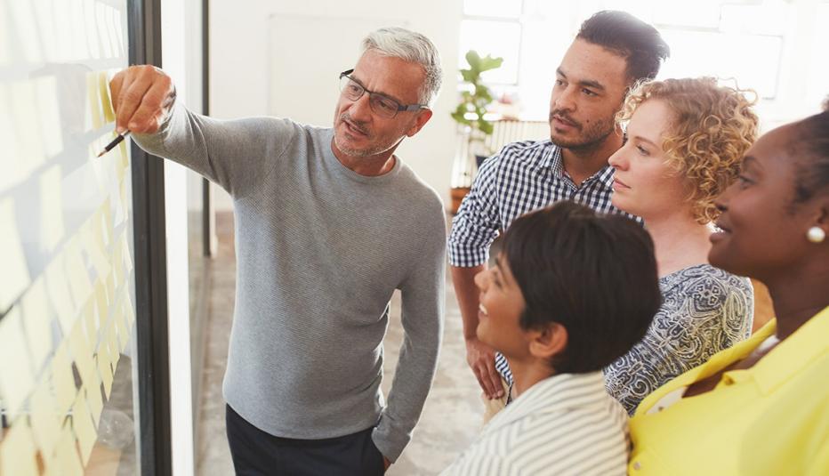 Mature businessman and his diverse team brainstorming with yellow adhesive notes on a glass wall in a bright modern office