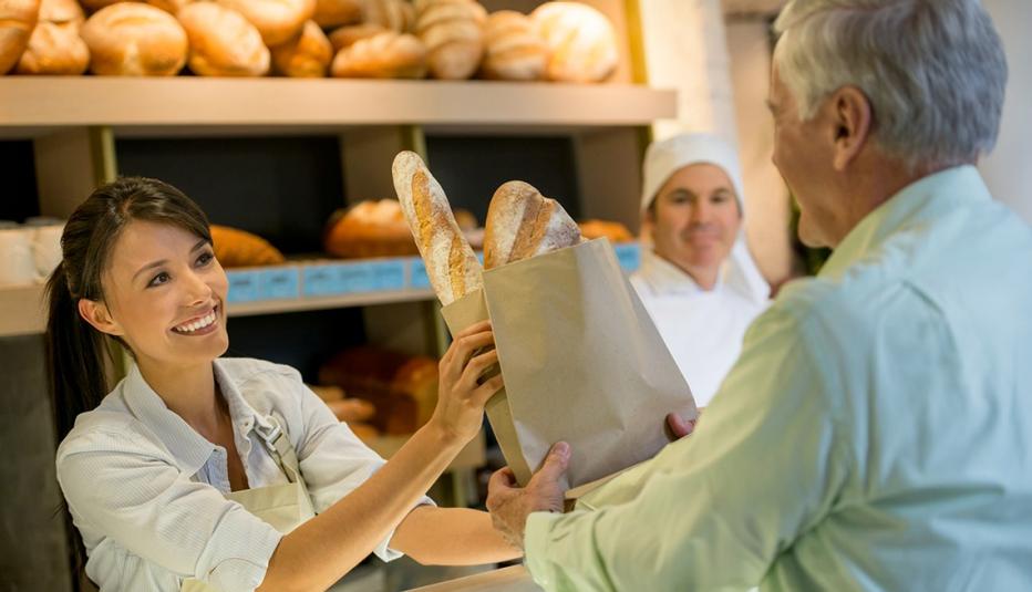 Woman at a bakery serving a man a bag of bread
