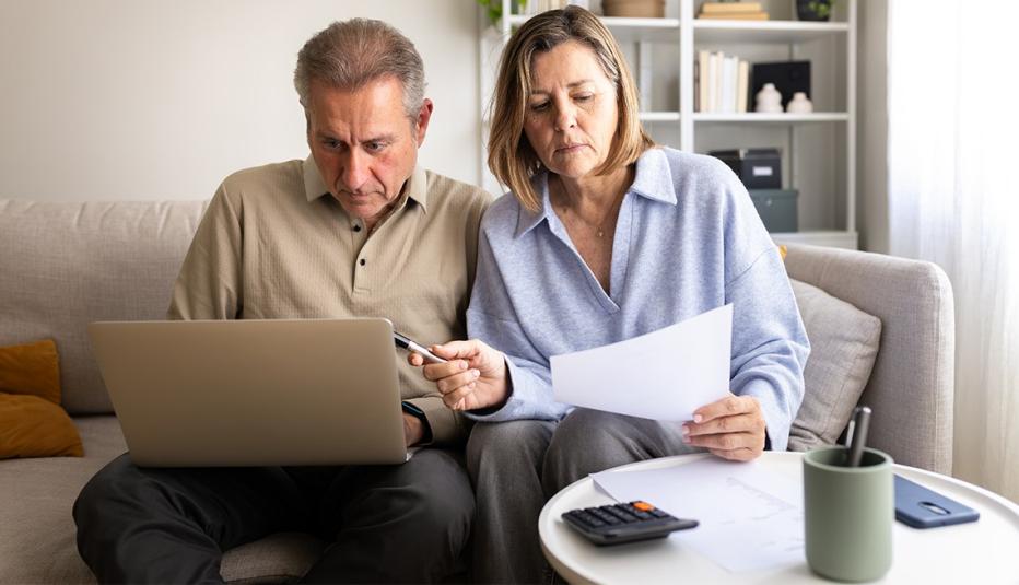 A caucasian couple works on paperwork and bills with their laptop in their living room.